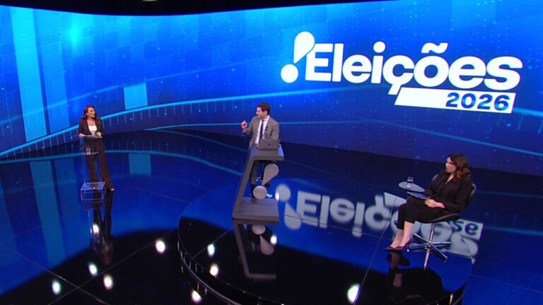 Jornalistas em estúdio da RedeTV! diante de painel com a inscrição Eleições 2026