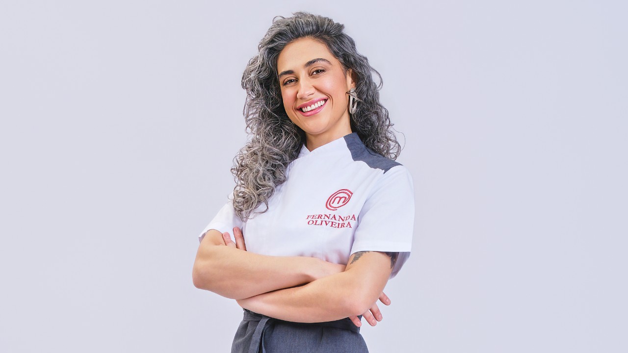Fernanda Oliveira sorri de braços cruzados com uniforme branco do MasterChef Profissionais