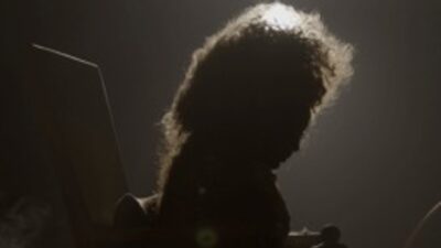 Imagem do documentário Elza mostra a silhueta de uma mulher com cabelos volumosos, iluminada por trás, em um ambiente escuro