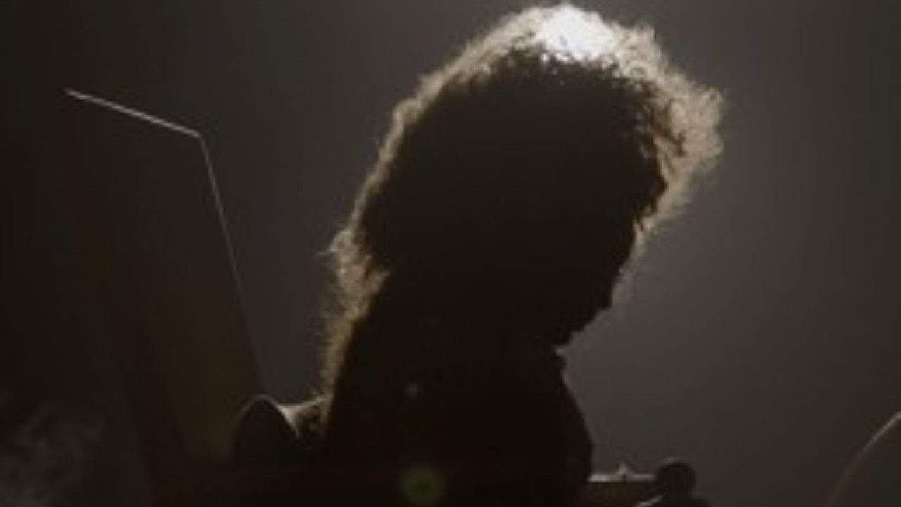 Imagem do documentário Elza mostra a silhueta de uma mulher com cabelos volumosos, iluminada por trás, em um ambiente escuro