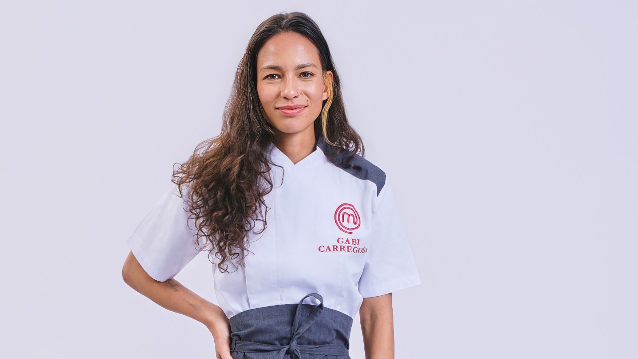 Gabriela Carregosa posa com uma mão na cintura e uniforme branco do MasterChef Profissionais