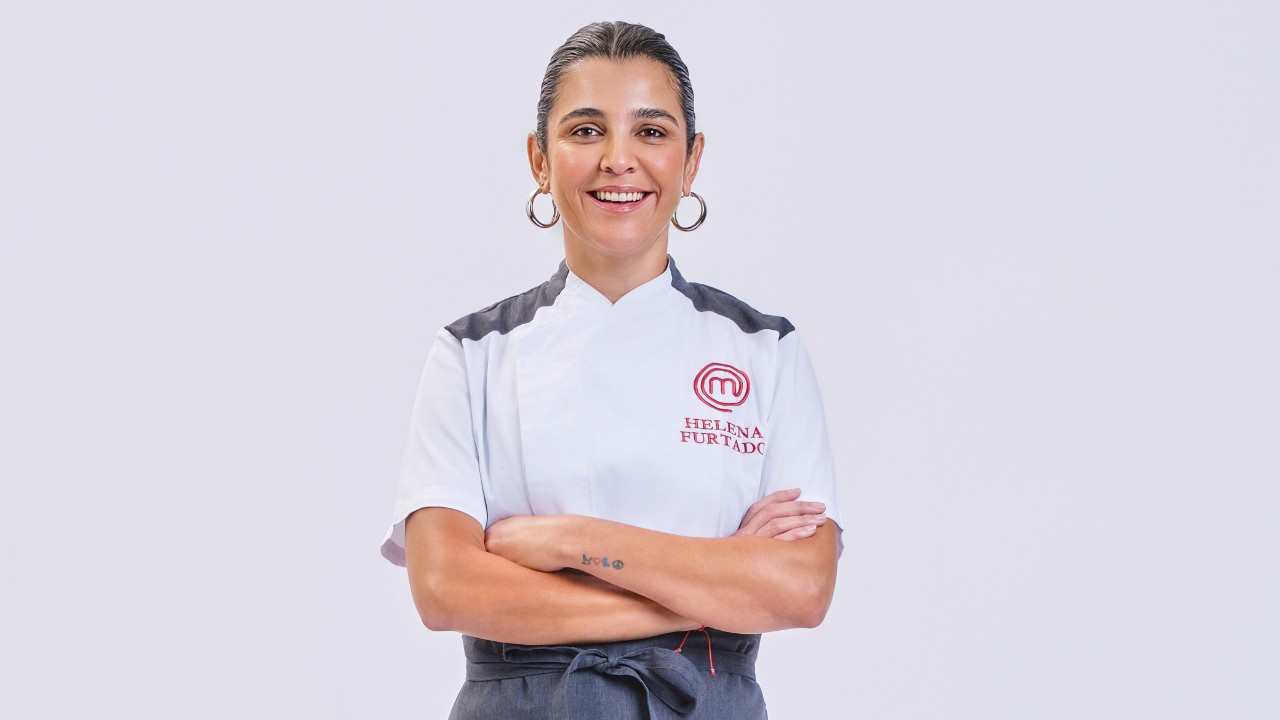 Helena Furtado sorri de braços cruzados com uniforme branco do MasterChef Profissionais