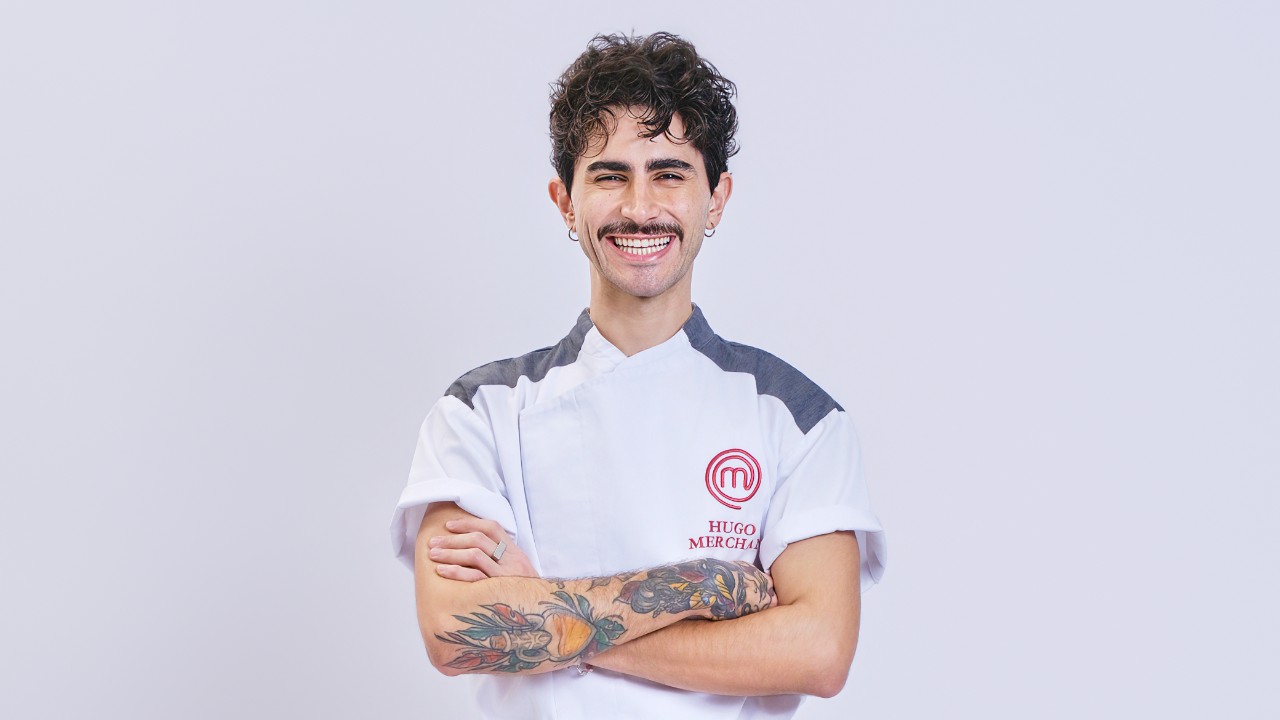 Hugo Merchan sorri de braços cruzados e exibe tatuagens com uniforme do MasterChef Profissionais