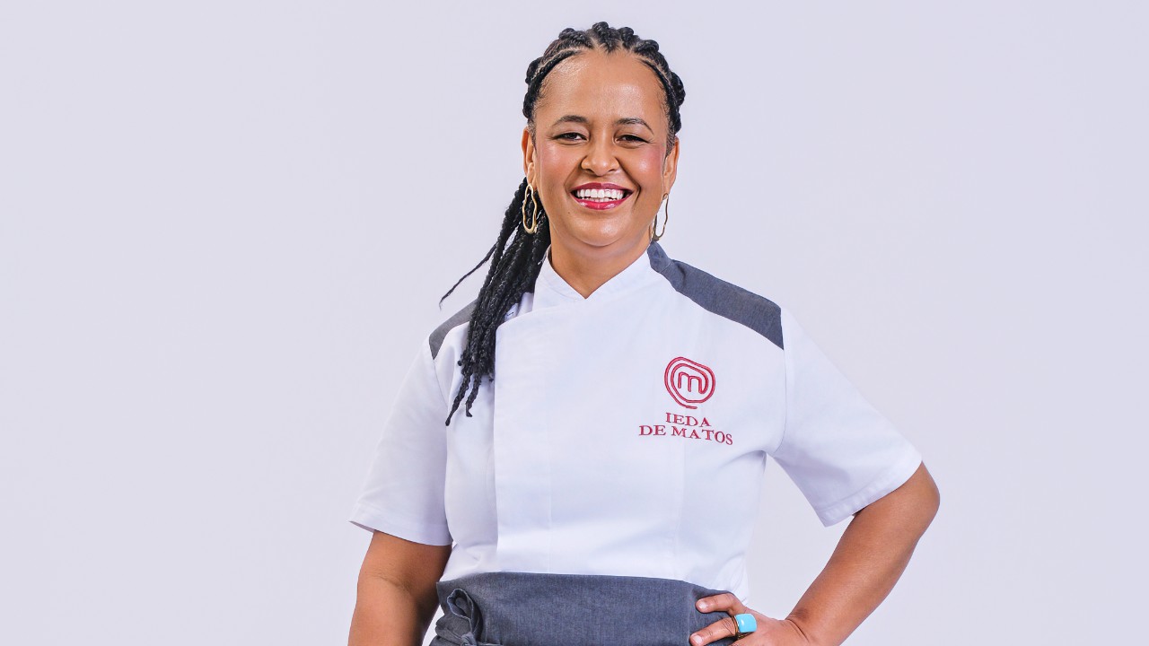 Ieda de Matos sorri com uma mão na cintura e uniforme branco do MasterChef Profissionais