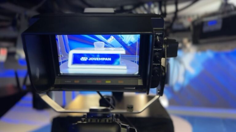 Monitor de câmera exibe bancada com logotipo da Jovem Pan em estúdio com iluminação azul