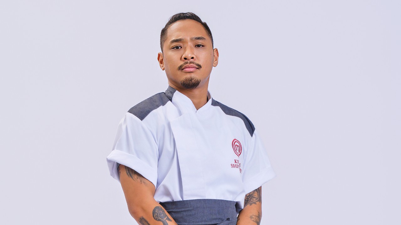 Kenzo Shintome posa com expressão séria e uniforme branco do MasterChef Profissionais