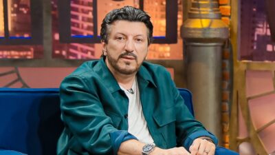 Lito Sousa de jaqueta verde e camiseta branca sentado em poltrona azul em estúdio de televisão