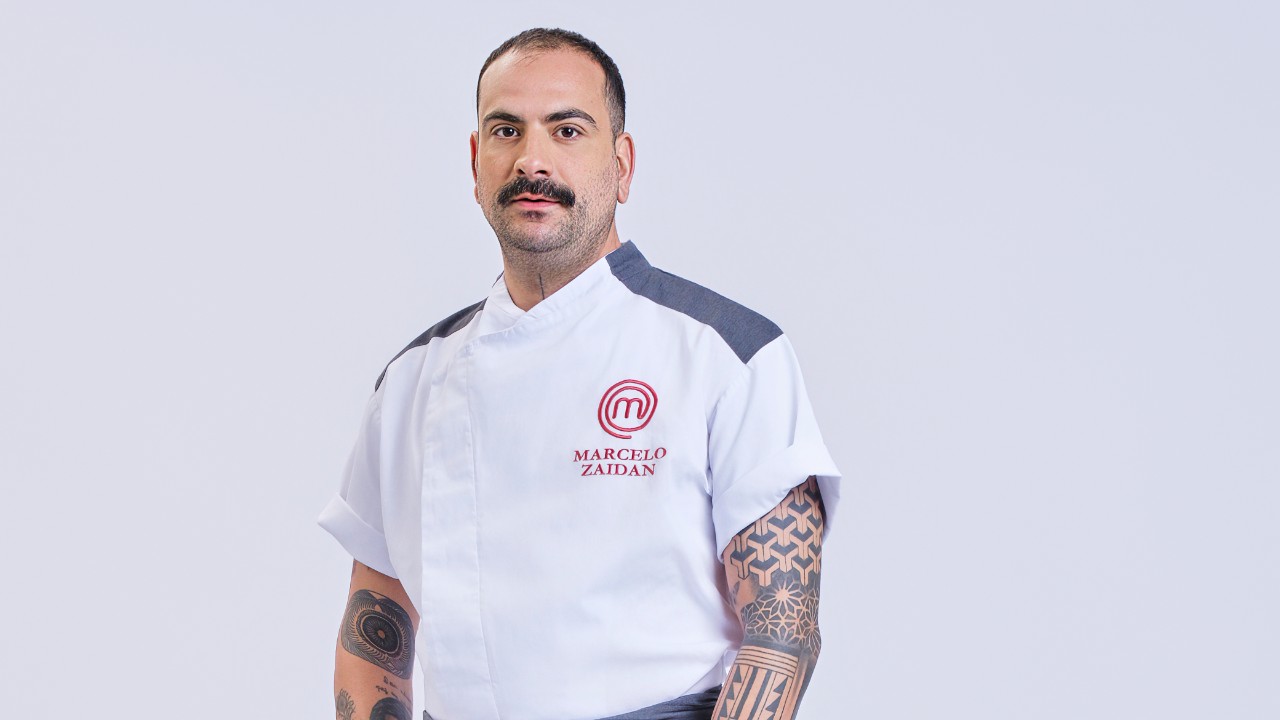 Marcelo Zaidan posa com tatuagens nos braços e uniforme branco do MasterChef Profissionais