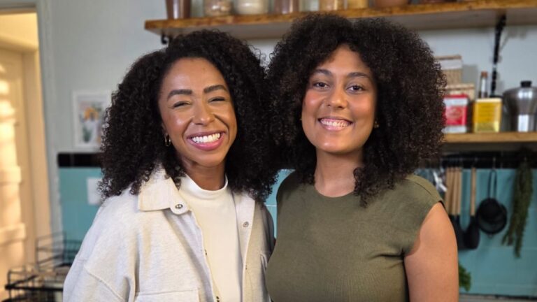 Mariana Bispo e Thallita Flor sorriem lado a lado em uma cozinha, com utensílios e potes ao fundo