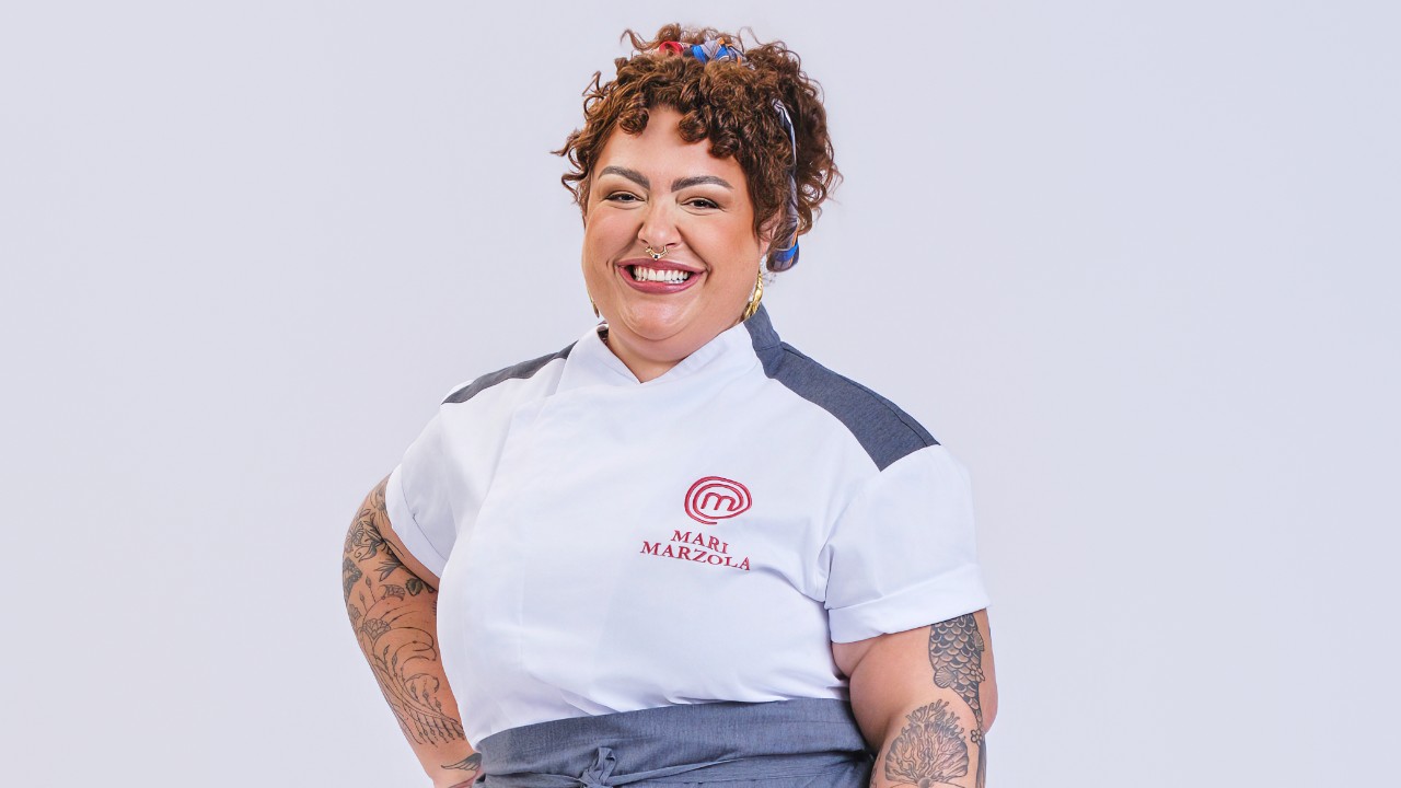 Mariana Marzola sorri com uma mão na cintura e uniforme branco do MasterChef Profissionais
