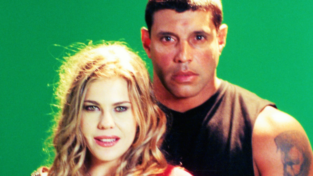 Marisol (Bárbara Paz) e Mário (Alexandre Frota) posam juntos diante de fundo verde na novela Marisol