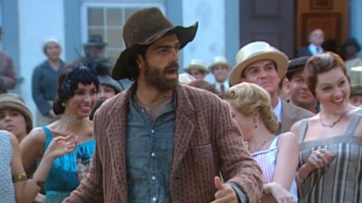 Petruchio (Eduardo Moscovis) aparece de chapéu marrom, barba e roupas rústicas, cercado por pessoas com trajes de época em cena da novela O Cravo e a Rosa