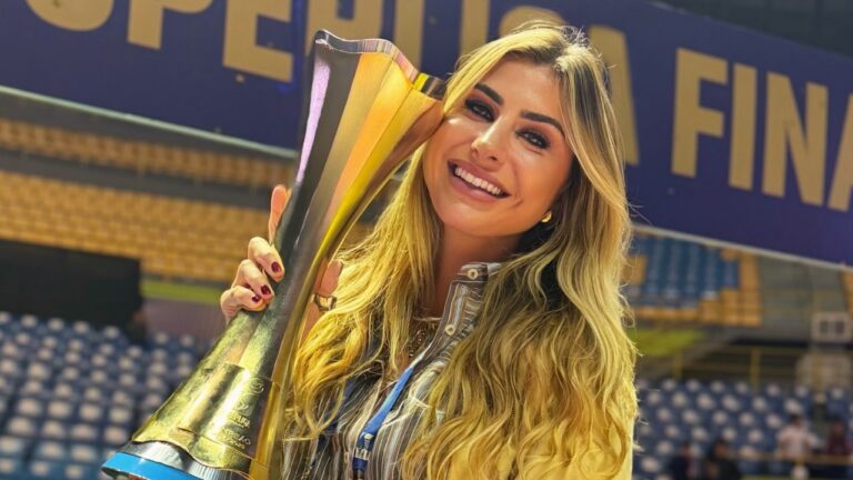 Renata Heilborn sorri com um troféu dourado junto ao rosto, diante das arquibancadas de um ginásio