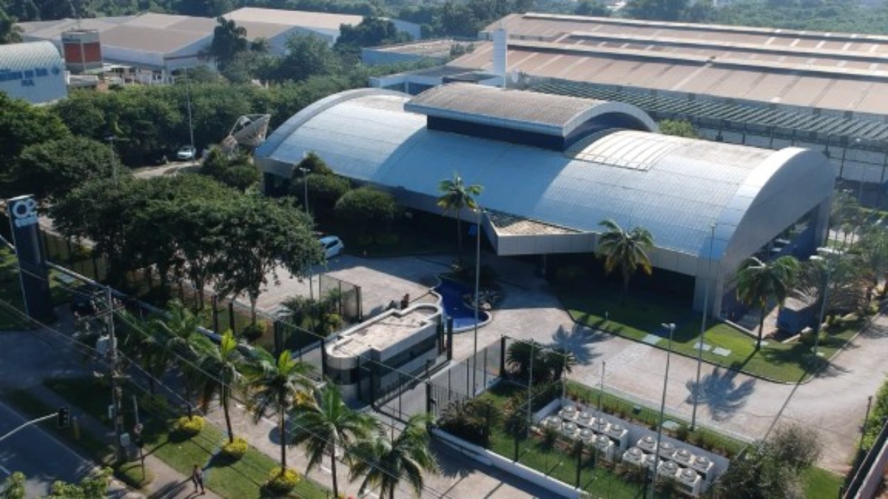 Vista aérea da sede da TV Tem, com prédios de cobertura curva, entrada principal, estacionamento e área arborizada