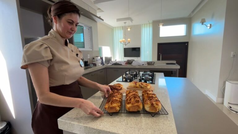 Mulher com uniforme de cozinha organiza pães recém-assados sobre uma grade de resfriamento em uma bancada