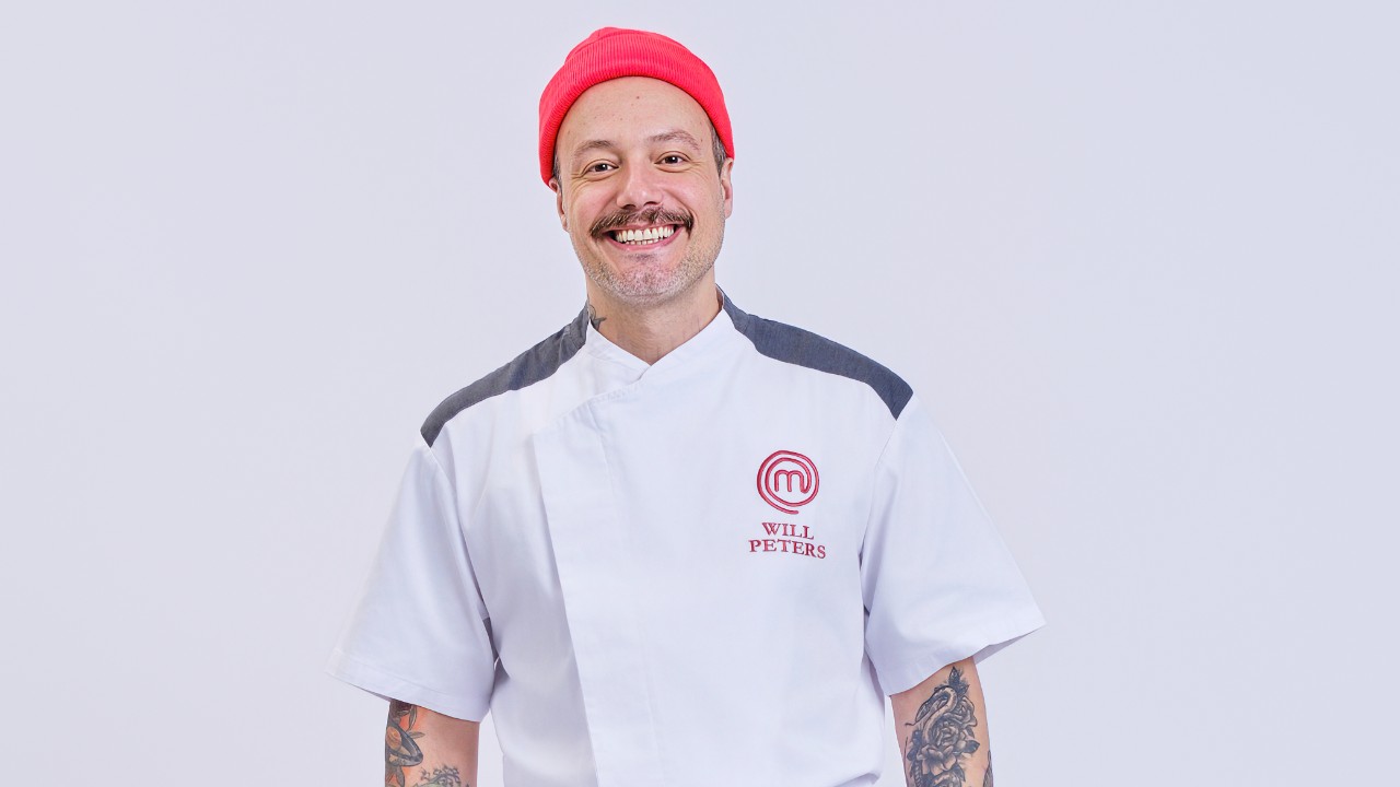 Willian Peters sorri de gorro vermelho e uniforme branco do MasterChef Profissionais
